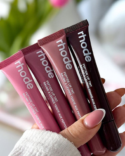 Four lip tint tubes from the brand 'rhode' held by a hand