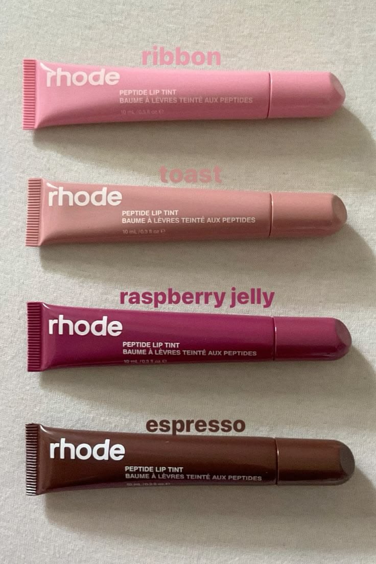 Four Rhode Peptide Lip Tint tubes arranged vertically on a light fabric background, labeled ribbon, toast, raspberry jelly, and espresso.
