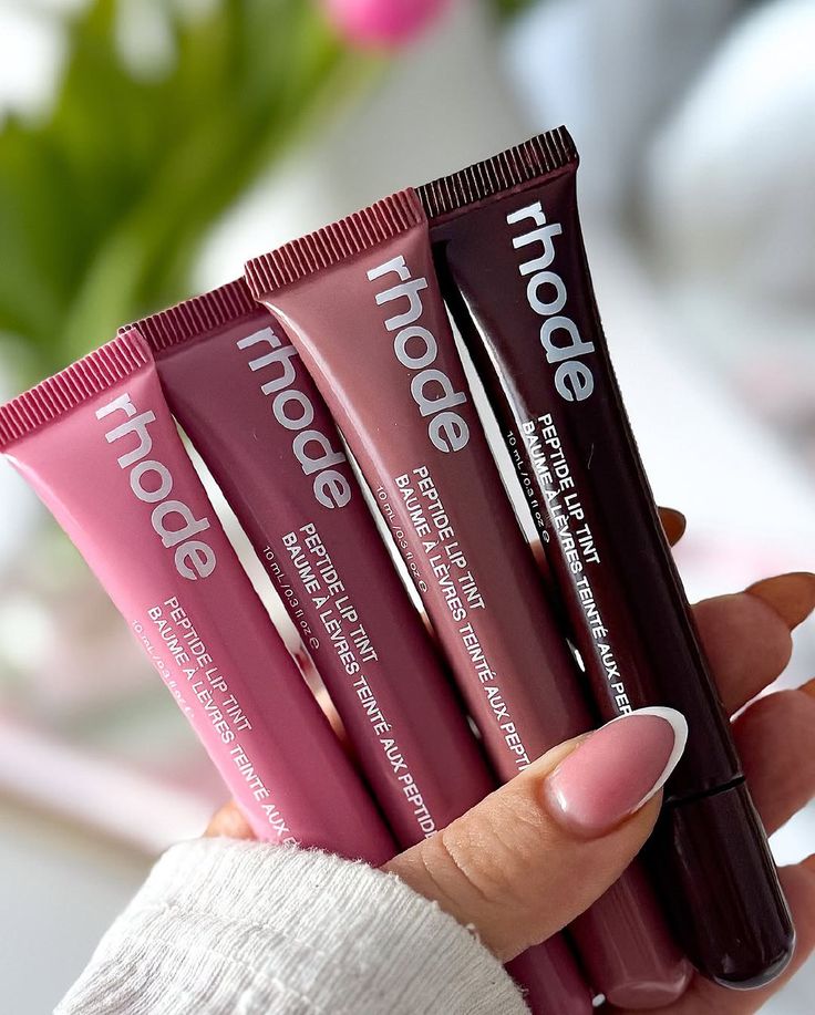 Four lip tint tubes from the brand 'rhode' held by a hand 
